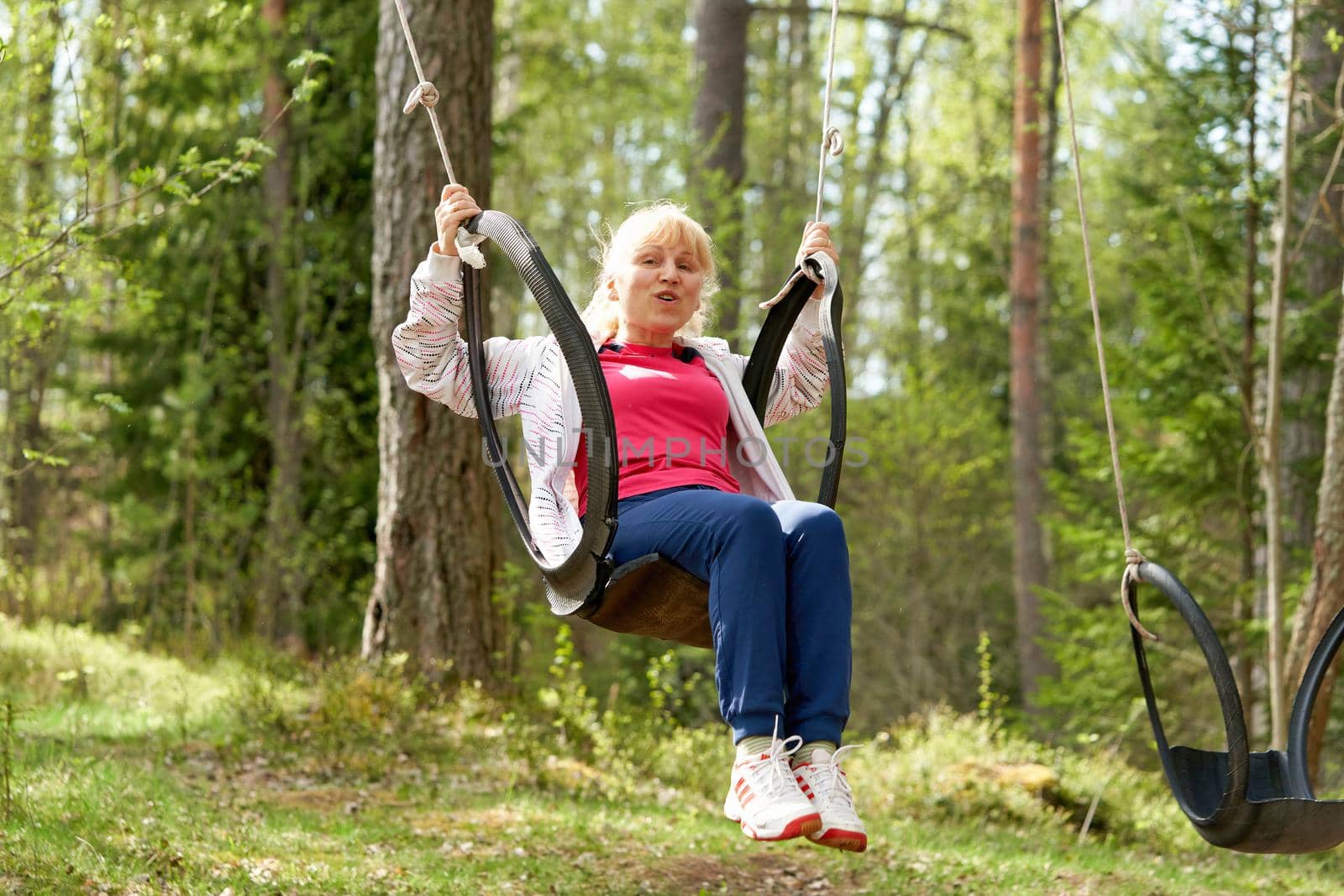 Middle aged woman in the woods swinging on a swing made from an old car tire by vizland