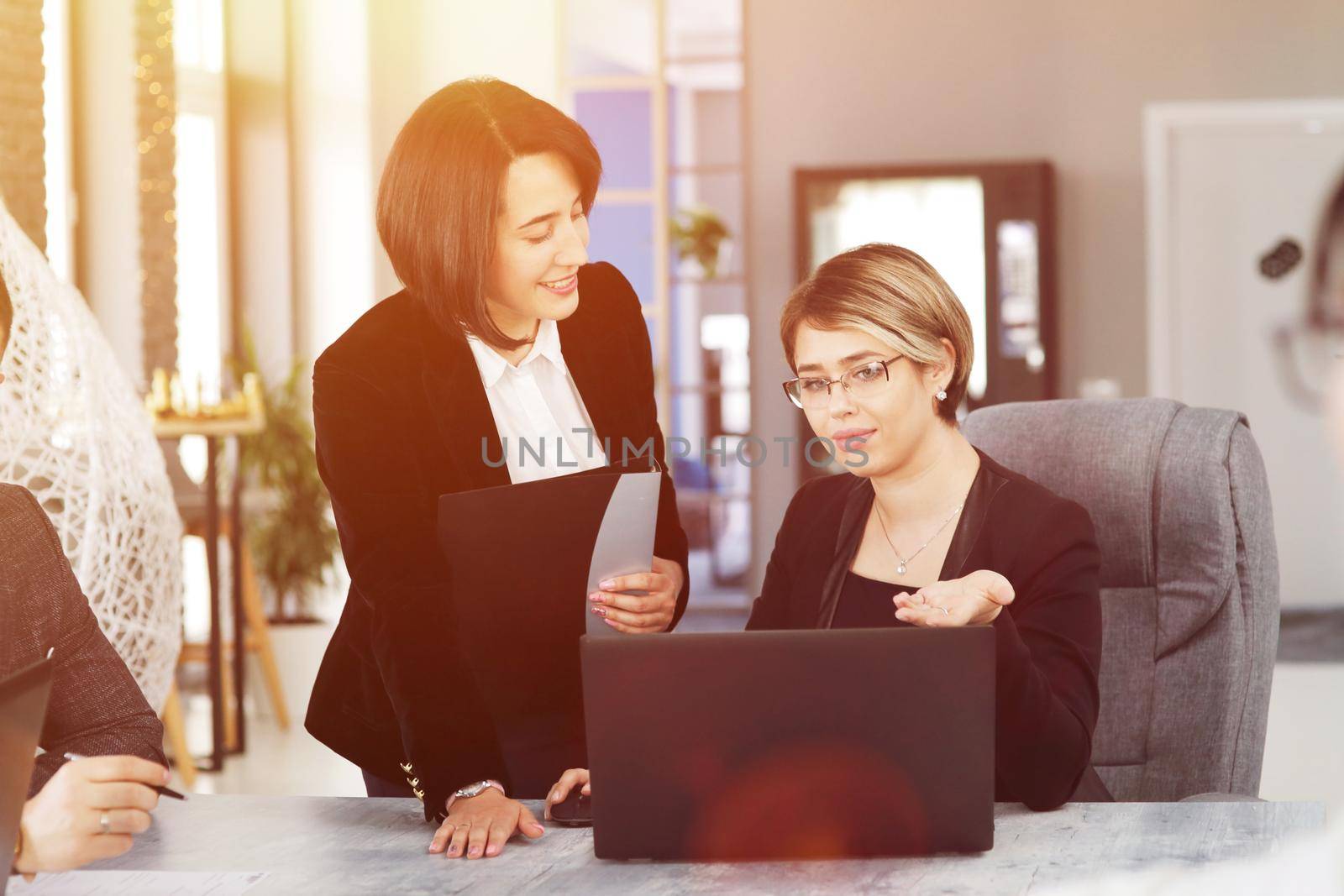 Two young business women in the office, analyzing information looking into a laptop, and smiling. 