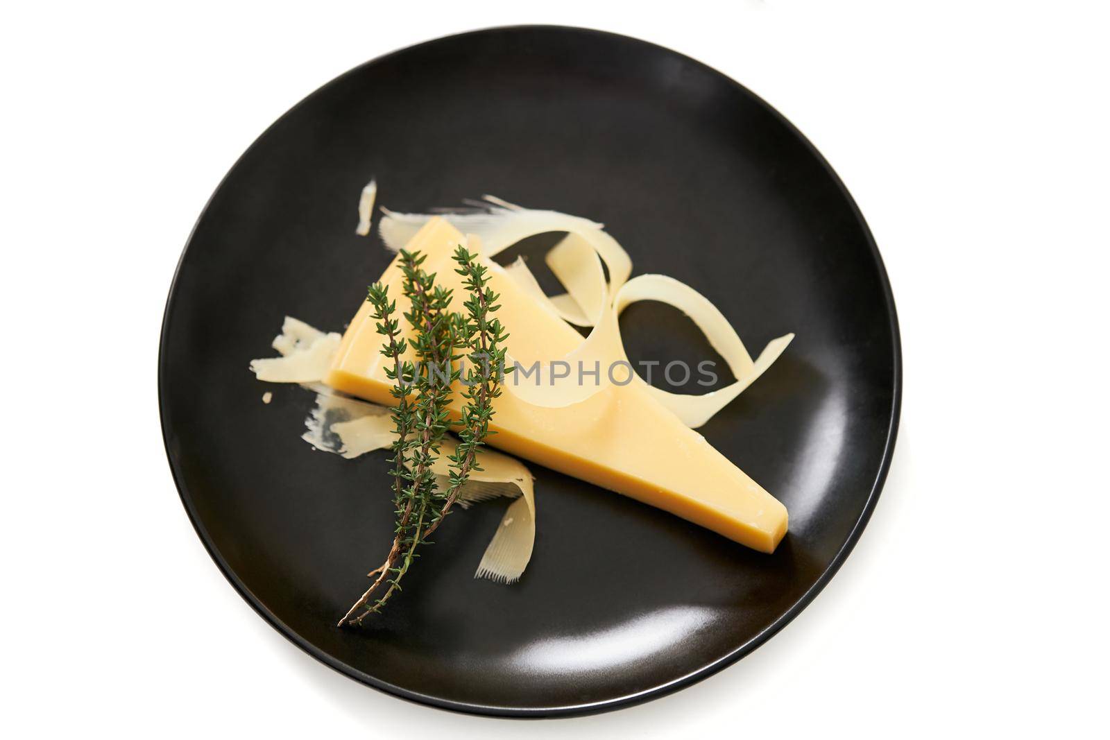 Top view of modern elegant black plate with juicy appetizing piece of cheese with sprig of rosemary on white background. Concept of delicious food with good composition. 