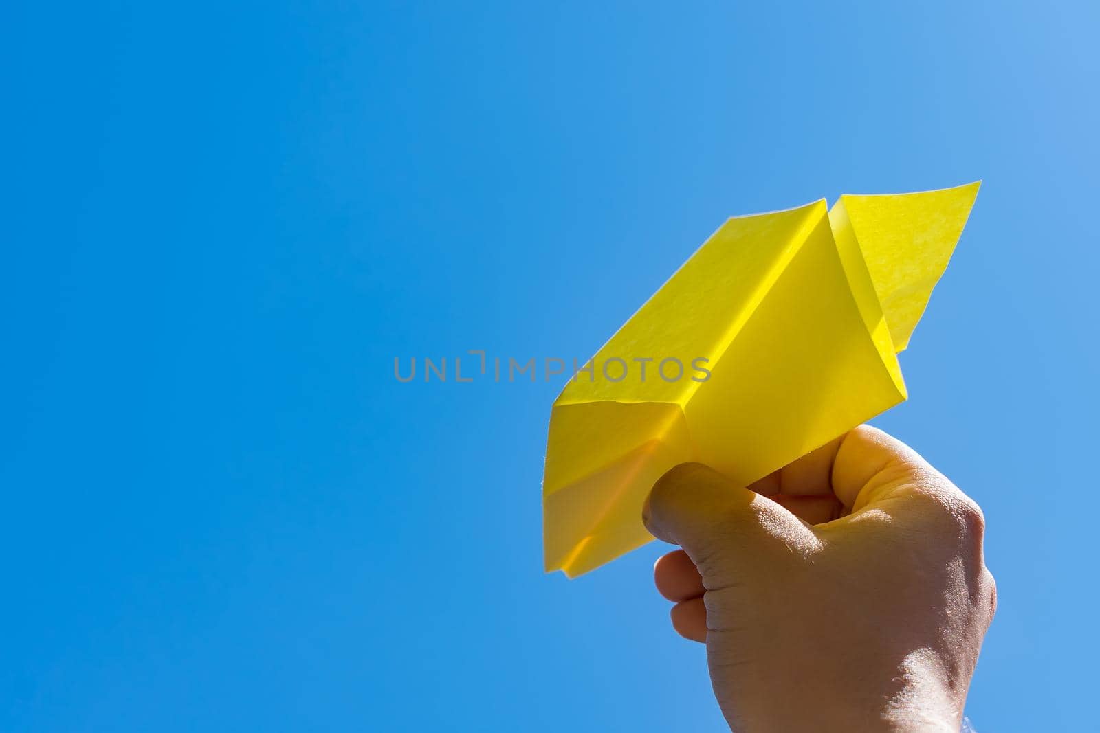 Launching a paper plane into a clear sky, as a symbol of peace and freedom, as well as success and a hobby. Man launches paper plane into the sky with hands close up