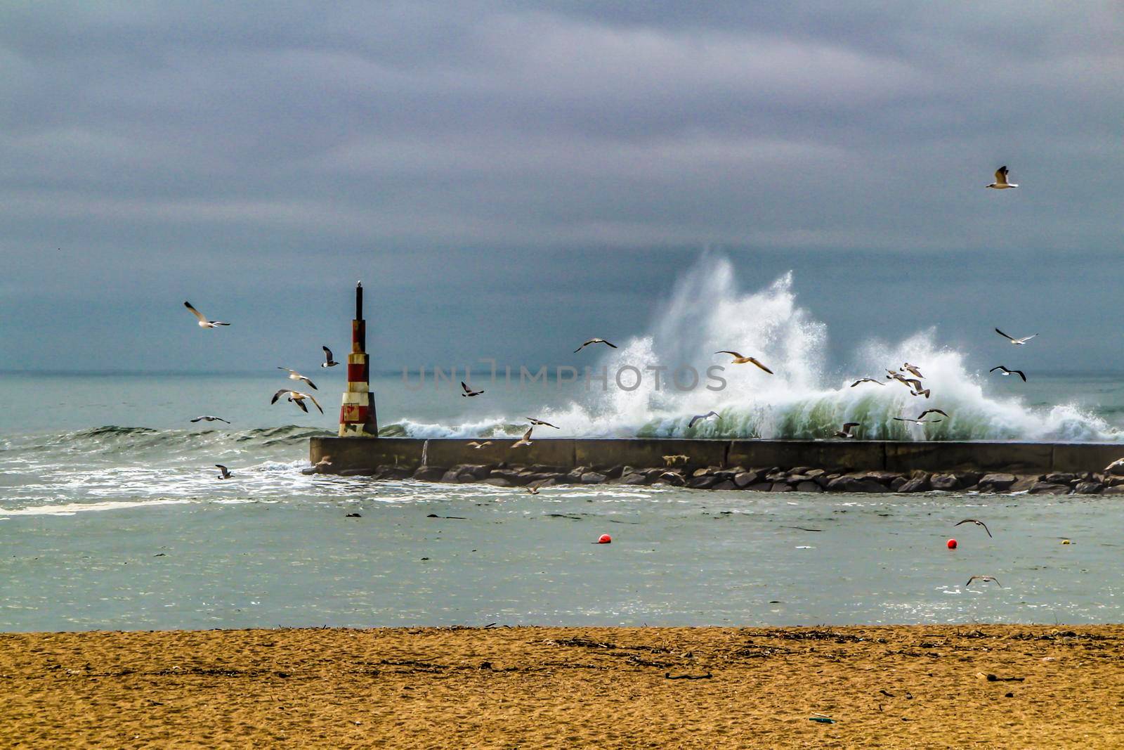 Giant waves breaking on the breakwater and the lighthouse on Aguda Beach, Miramar, Arcozelos town