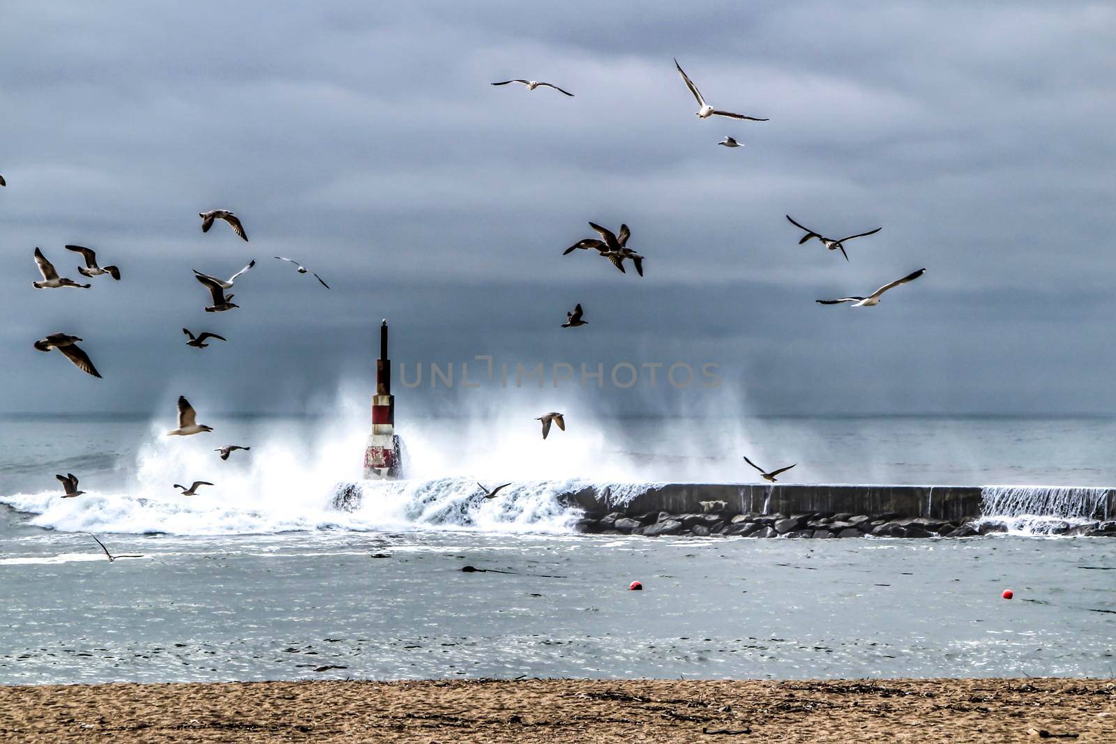 Giant waves breaking on the breakwater and the lighthouse on Aguda Beach, Miramar, Arcozelos town