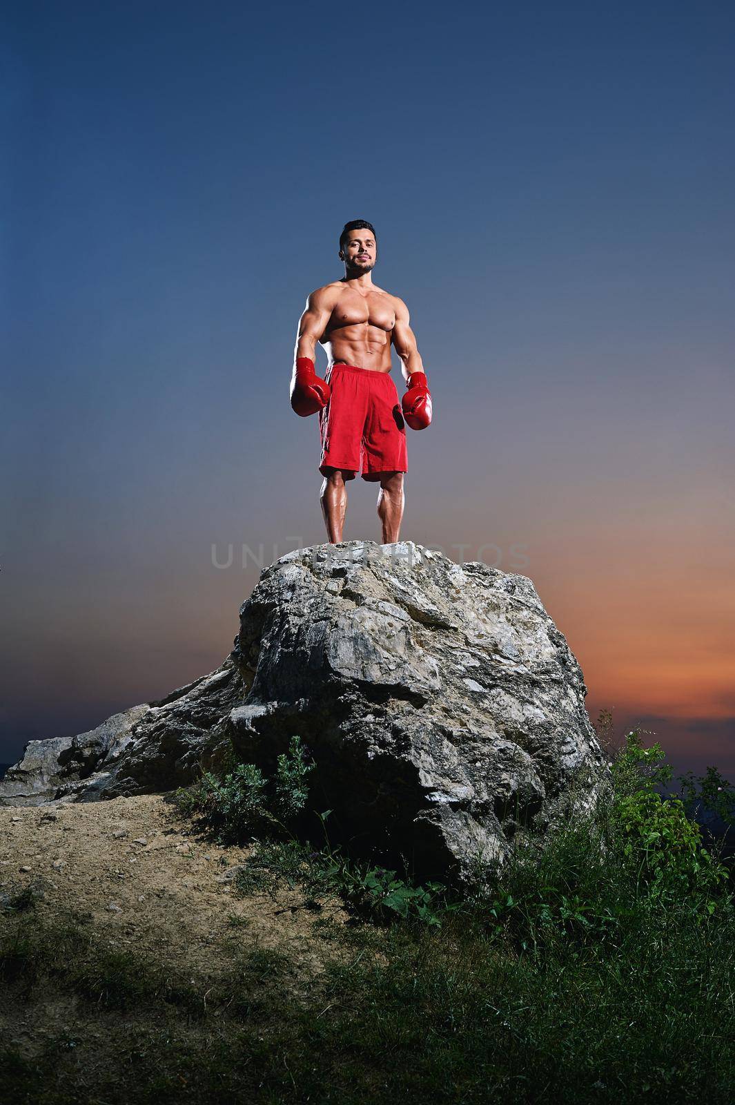 Young muscular male fighter wearing boxing gloves standing in a stance on a rock outdoors on sunset copyspace people lifestyle sports athletics sportsman fitness muscles combat martial fighting.
