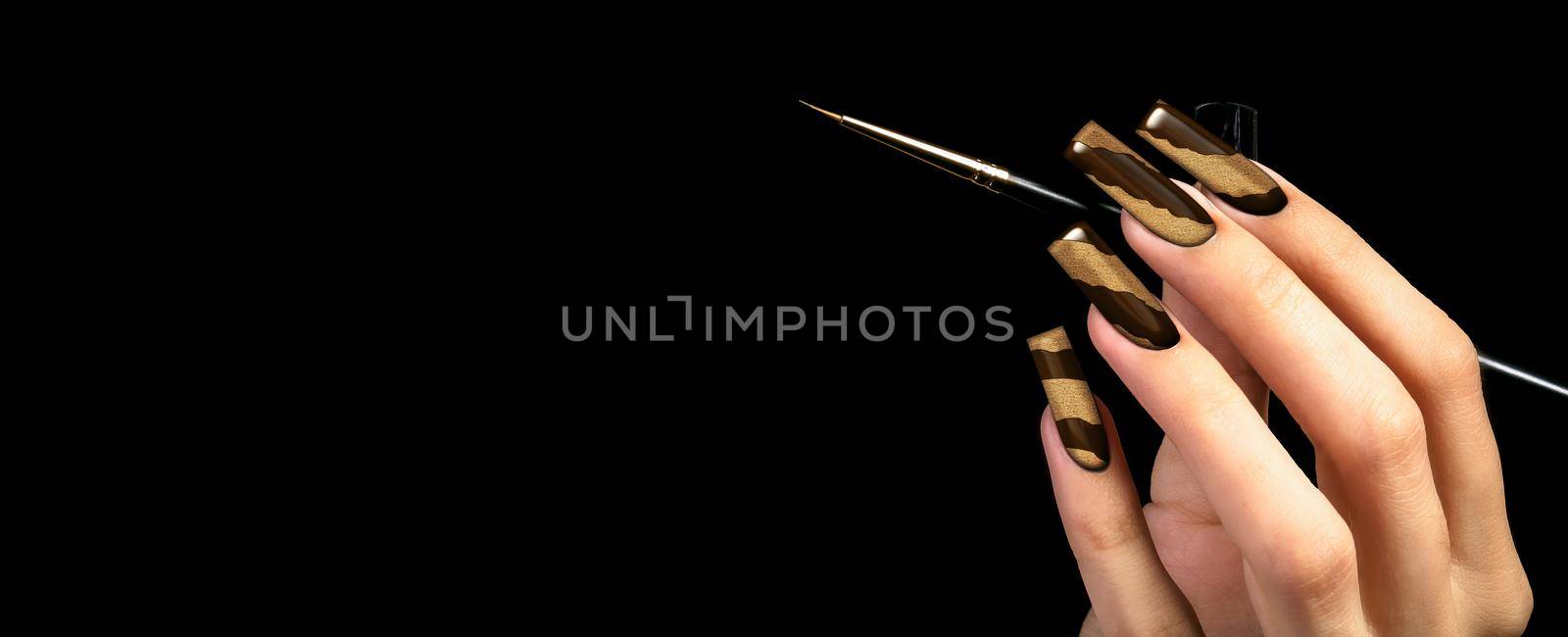Hand with a beautiful manicure and a brush on a black background. Nail design. Extended nails.