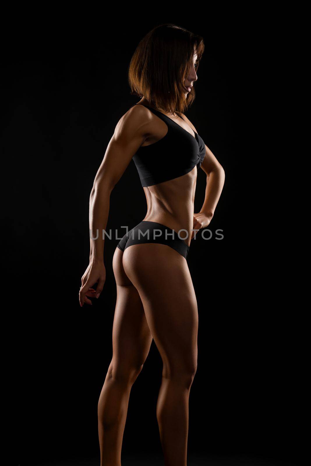 Body of work. Vertical shot of a fitness woman with perfect body posing against dark background