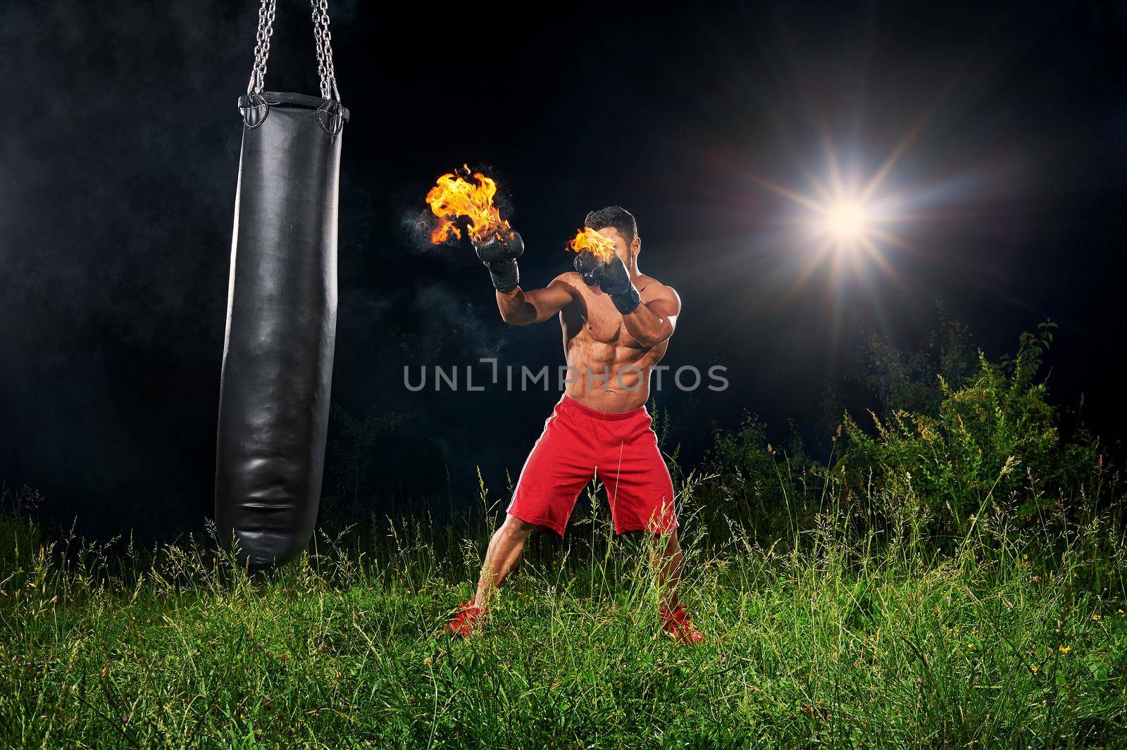 Shot of a powerful aggressive fighter with muscular strong body working out at night outdoors with his boxing gloves burning with fire copyspace sport power strength force effort activity sportsman.