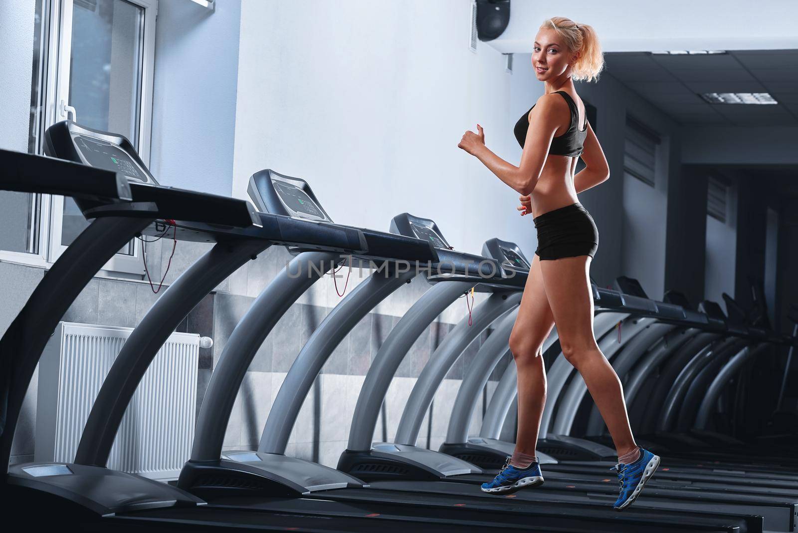 Young beautiful athletic woman running on a treadmill at the gym by SerhiiBobyk