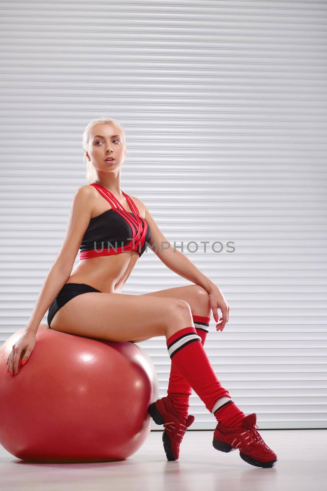 Beautiful young sporty girl wearing sports top and shorts sitting on a fitness ball after her workout relaxation confidence fit toned muscular abs sexy hot lifestyle physique personal trainer gym .