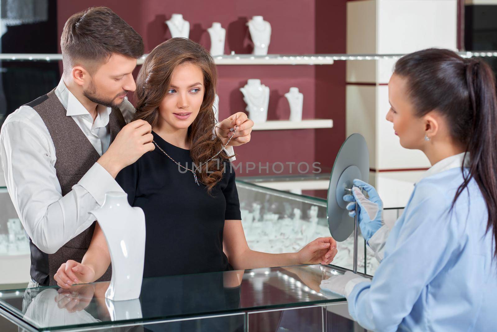 I think I like it. Professional jeweler standing with a young loving couple fitting a necklace at the store couple buying jewelry profession luxury lifestyle festive anniversary present couple love