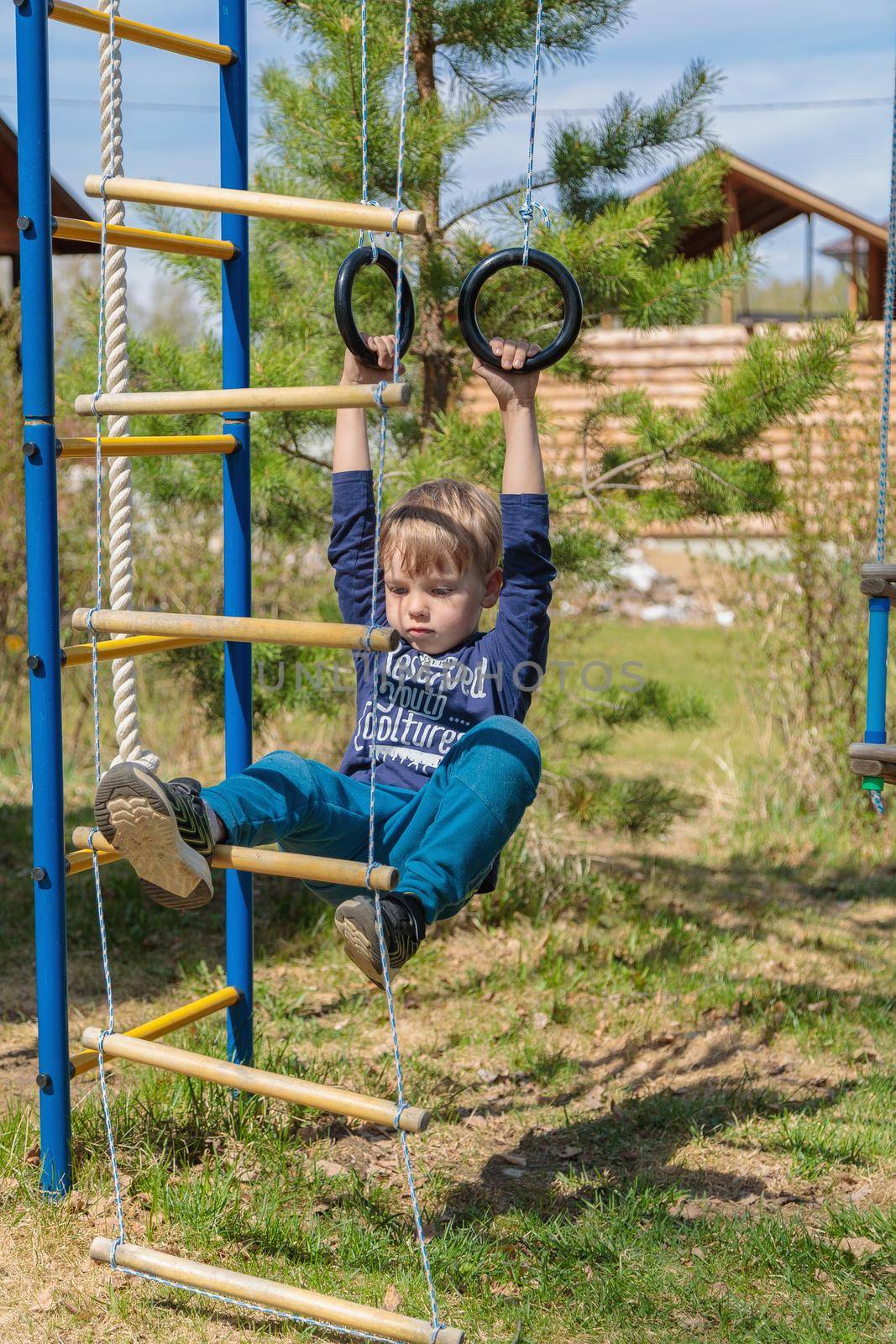 A blonde-haired child is playing on the playground, hanging on rings by Yurich32