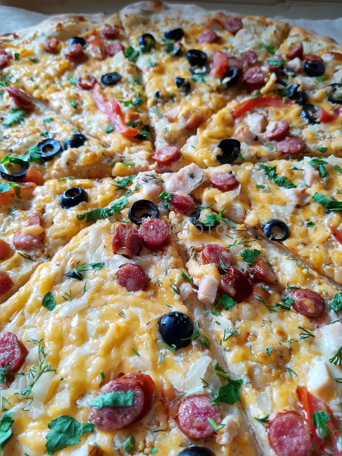 Sliced large pizza lies on the table close-up.