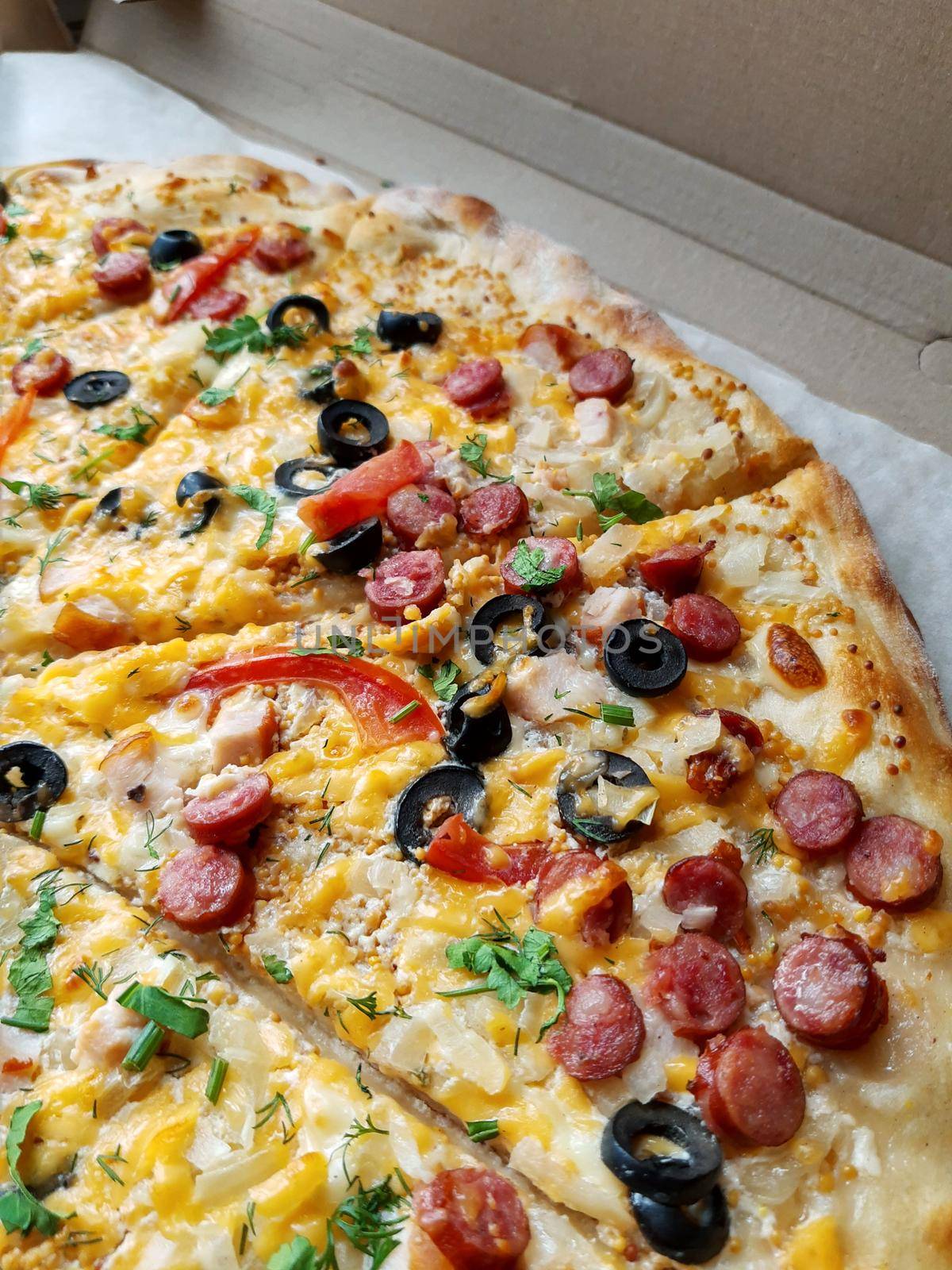 Sliced large pizza lies on the table close-up.