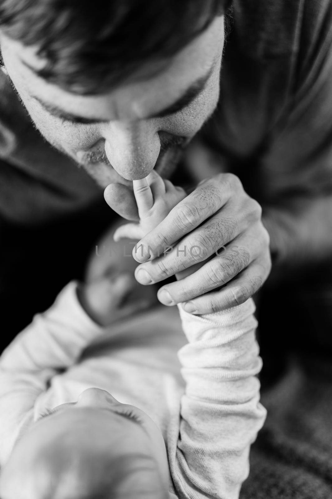 Dad kisses his baby's tiny hands. Close-up. Black and white photo by Nadtochiy