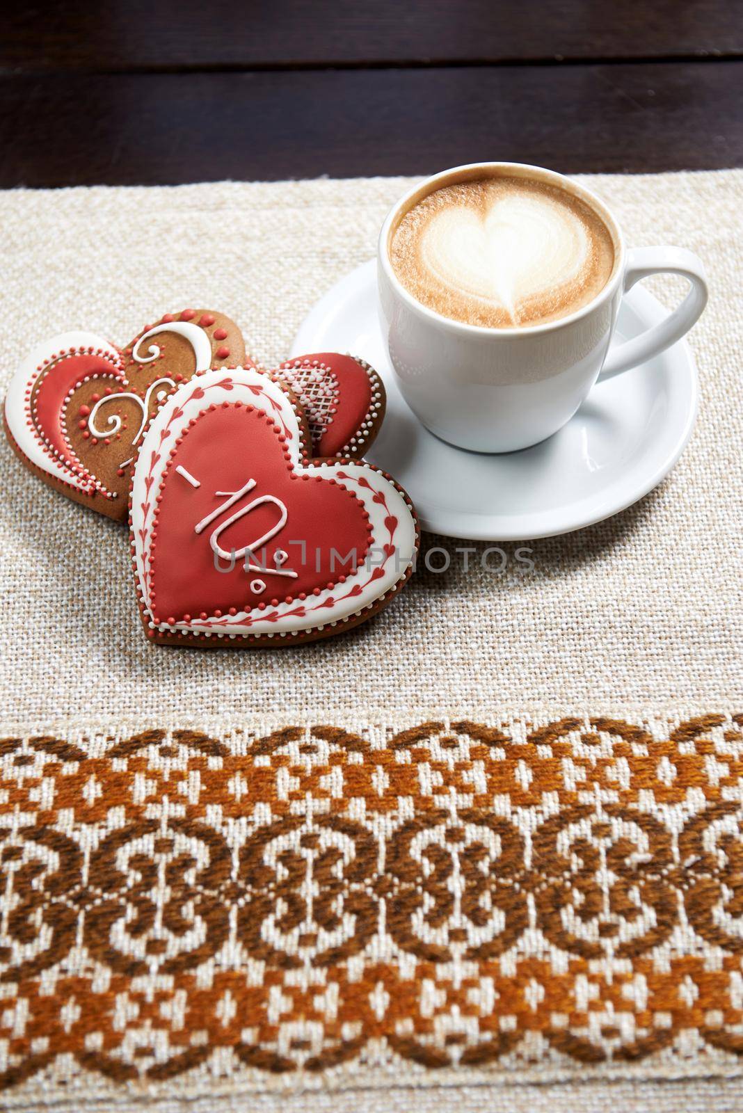 Cup of a perfection. High angle shot of a cup of coffee with froth design and three glazed red Valentine s day cookies on the table