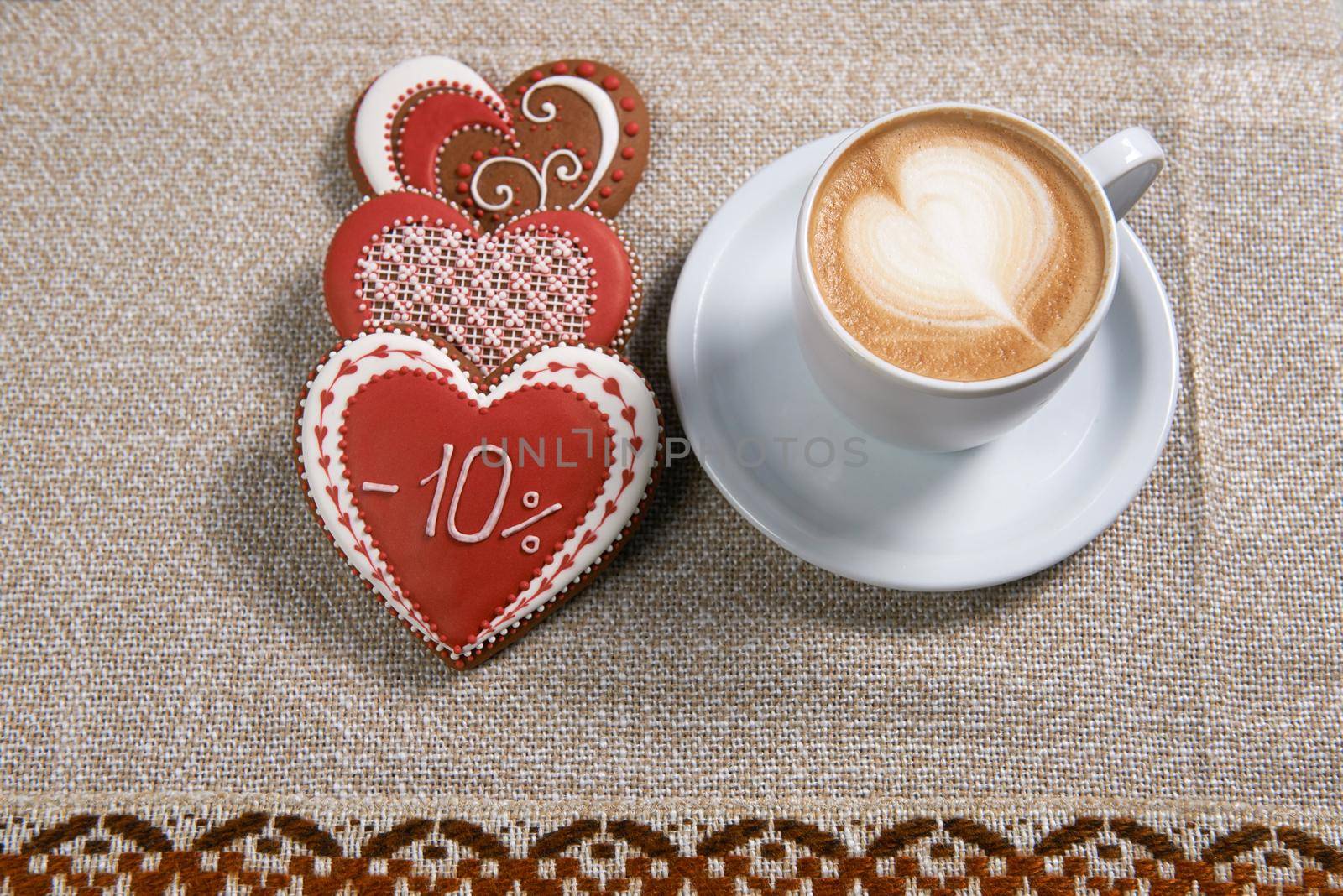 Have a cozy morning. Top view shot of a cup of cappuccino placed near three heart shaped Valentine cookies