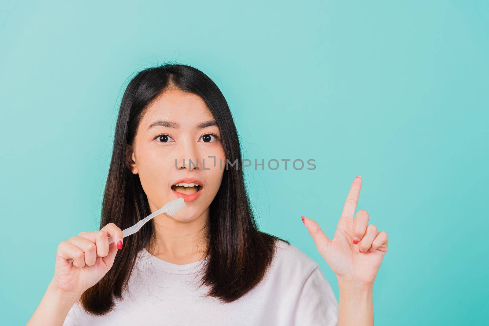woman teen smiling holding toothbrush brushing teeth in the morning pointing finger to empty space by Sorapop