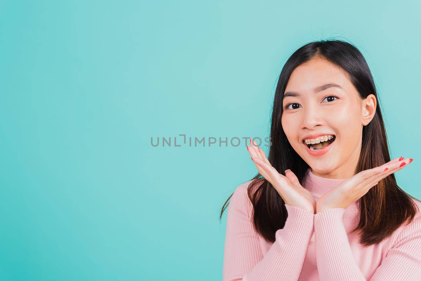 Happy young Asian beautiful woman smiling wear silicone orthodontic retainers on teeth surprised she is excited screaming and raise hand make gestures wow, studio shot isolated on blue background