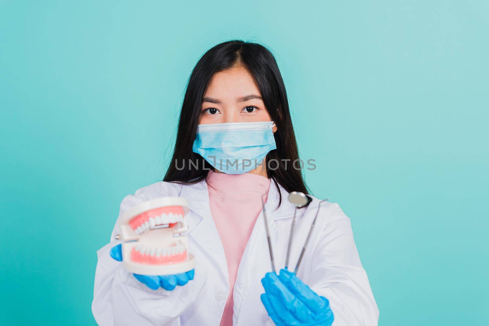 Asian beautiful woman dentist holding professional tool and model teeth denture, female doctor checking denture studio shot isolated on blue background. Dental hygiene surgery health care concept