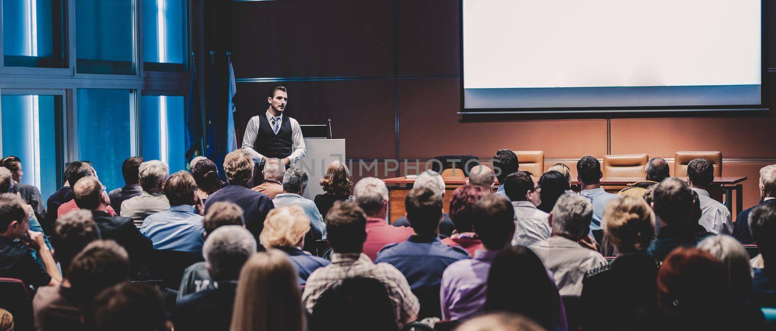 Speaker giving a talk in conference hall at business meeting event. Rear view of unrecognizable people in audience at the conference hall. Business and entrepreneurship concept.