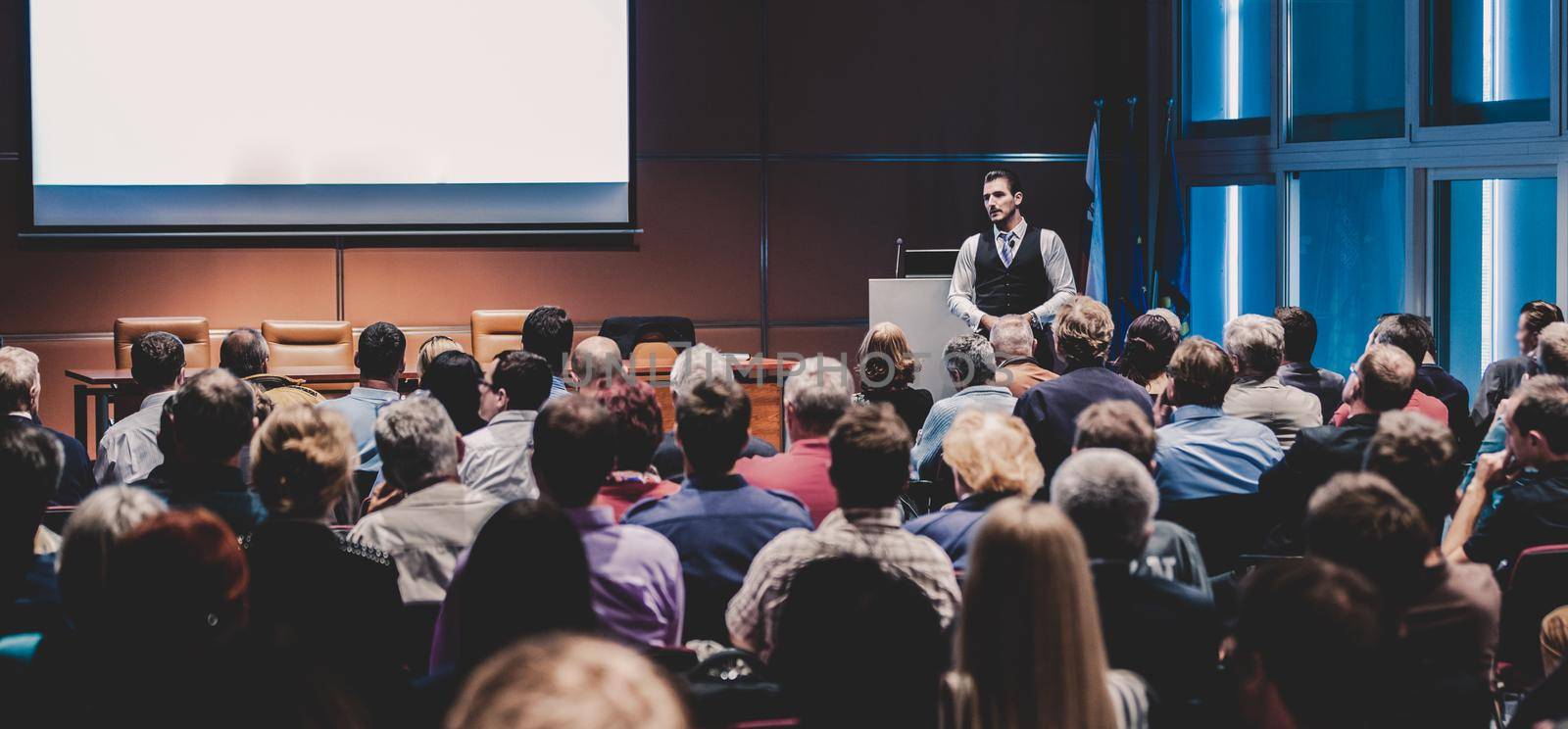 Speaker giving a talk in conference hall at business meeting event. Rear view of unrecognizable people in audience at the conference hall. Business and entrepreneurship concept.