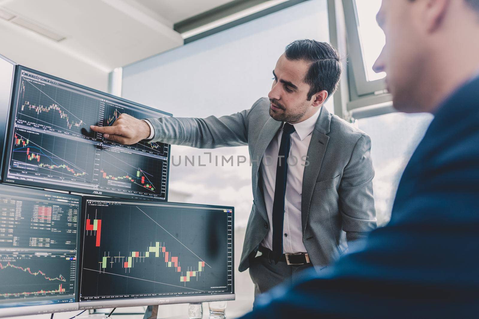 Businessmen trading stocks online. Stock brokers looking at graphs, indexes and numbers on multiple computer screens. Colleagues in discussion in traders office. Business success concept.