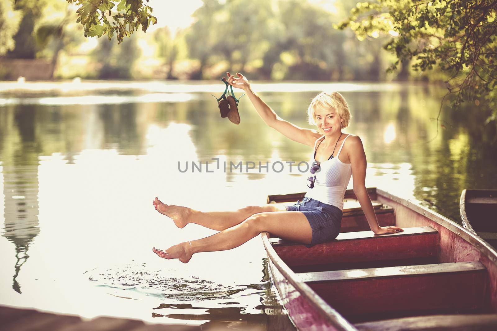Carefree young blonde woman enjoying the sunny summer day on a vintage wooden boats on a lake in pure natural environment on the countryside.
