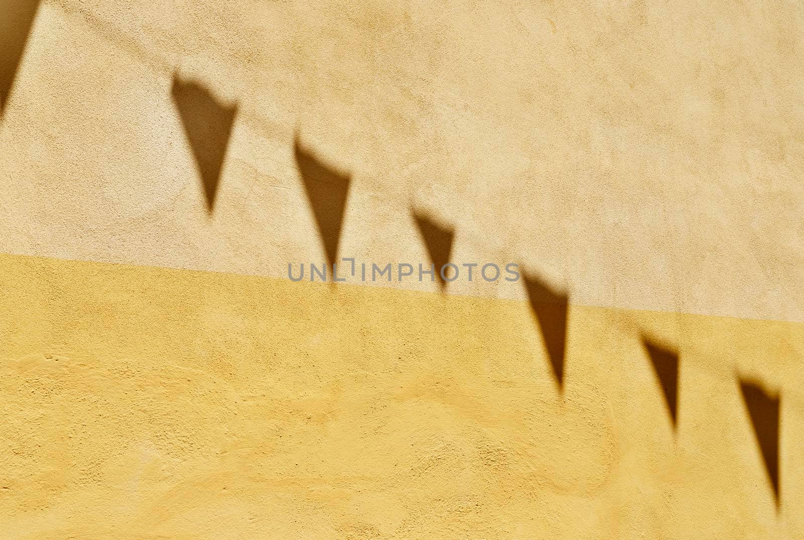 Shadows of bunting flags on yellow wall in a bright day