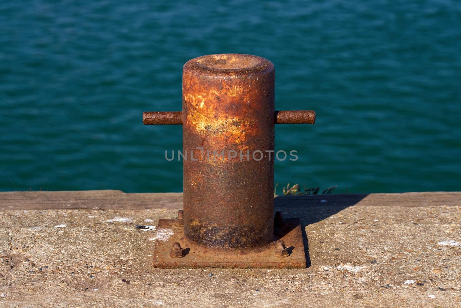 The heavy steel pillar bollard is mounted on a harbour wall for securing boats while docking in port.