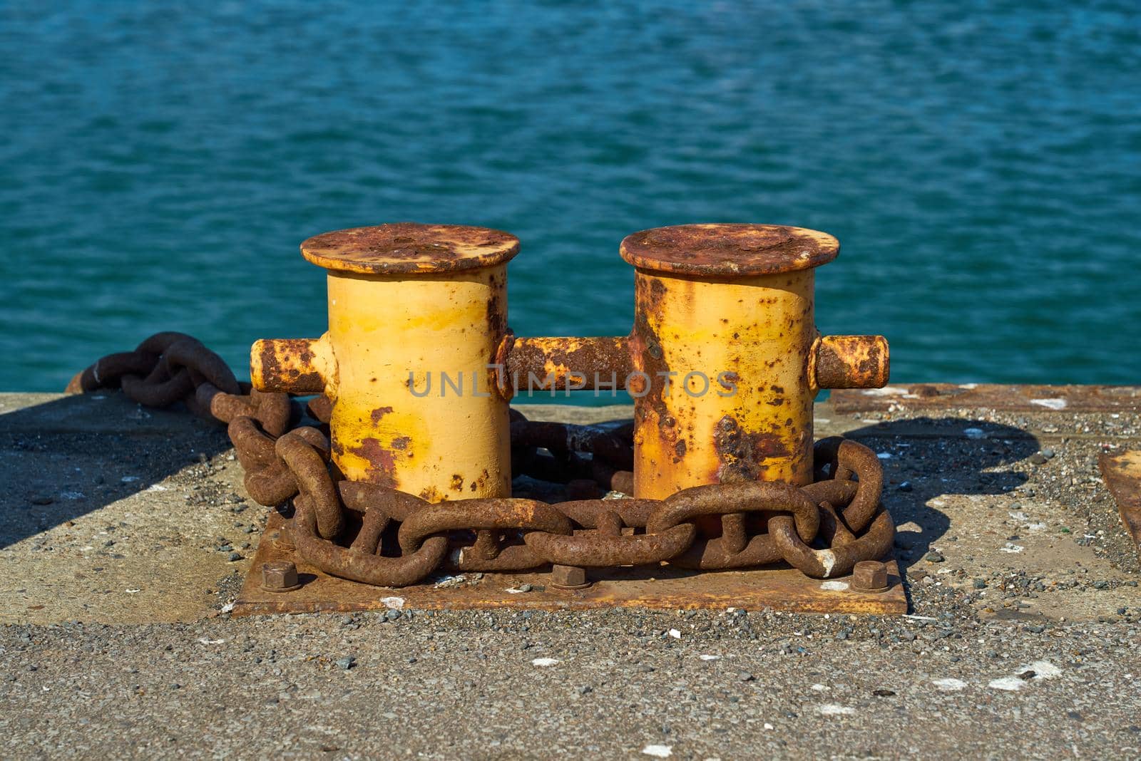 A double bitt mooring bollard with a heavy chain around it. by ChrisWestPhoto