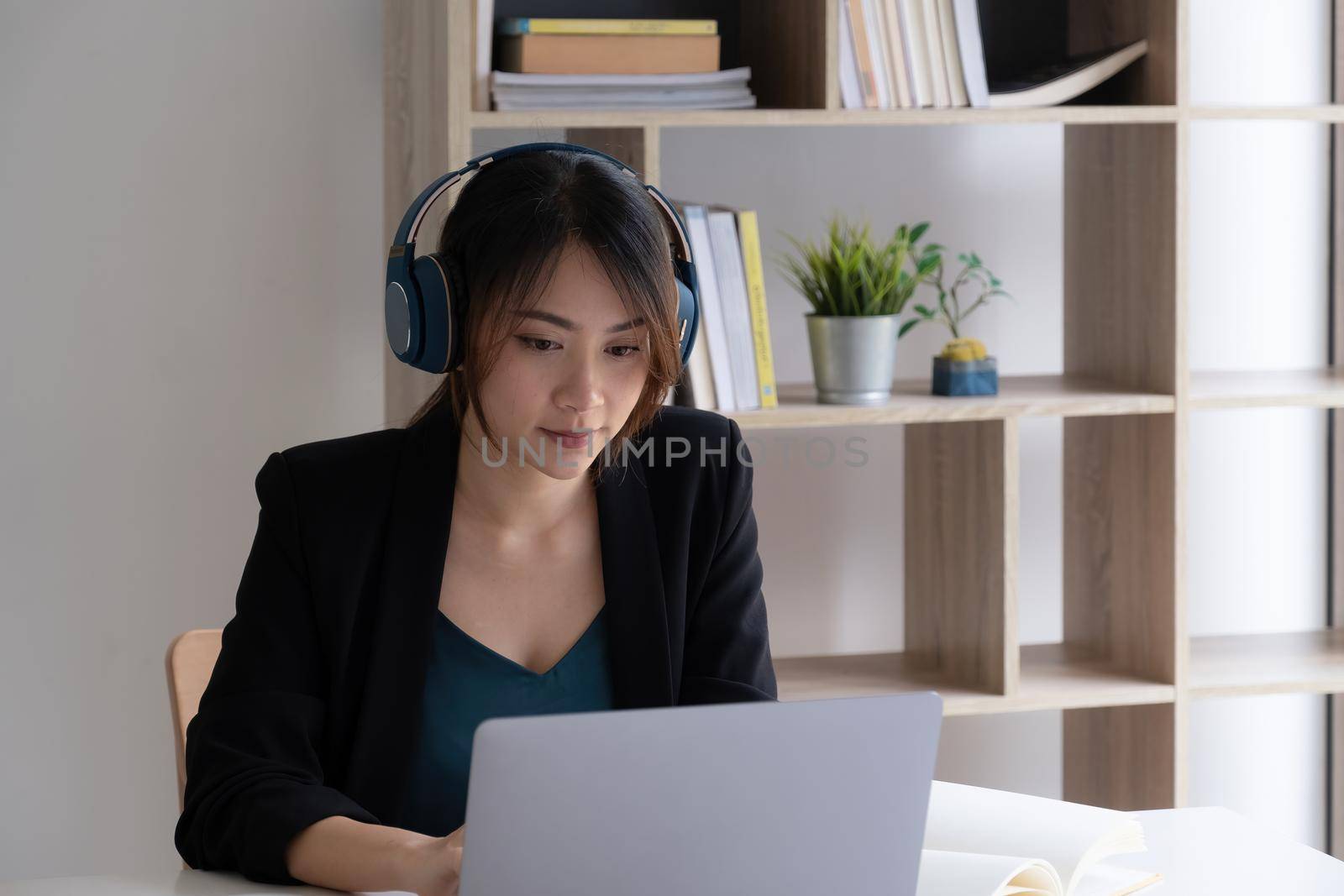A woman with headphones concentrates on a webinar on her laptop computer