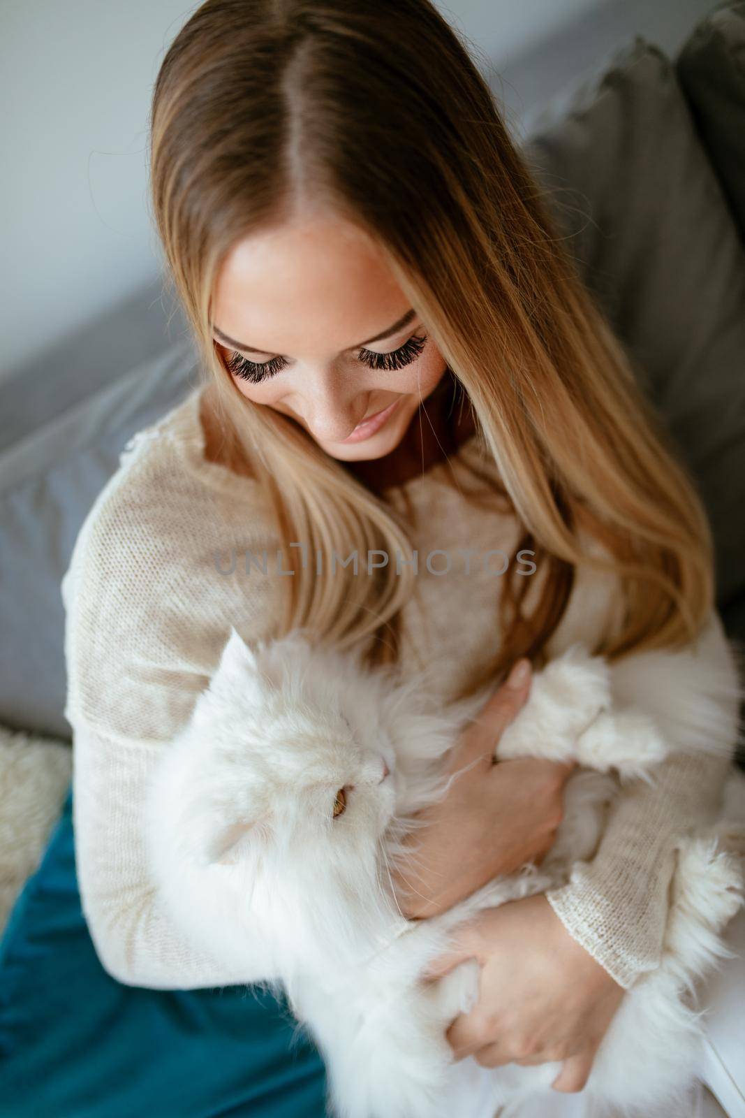 Cute young woman relaxing at home and embracing her beautiful white Persian cat.