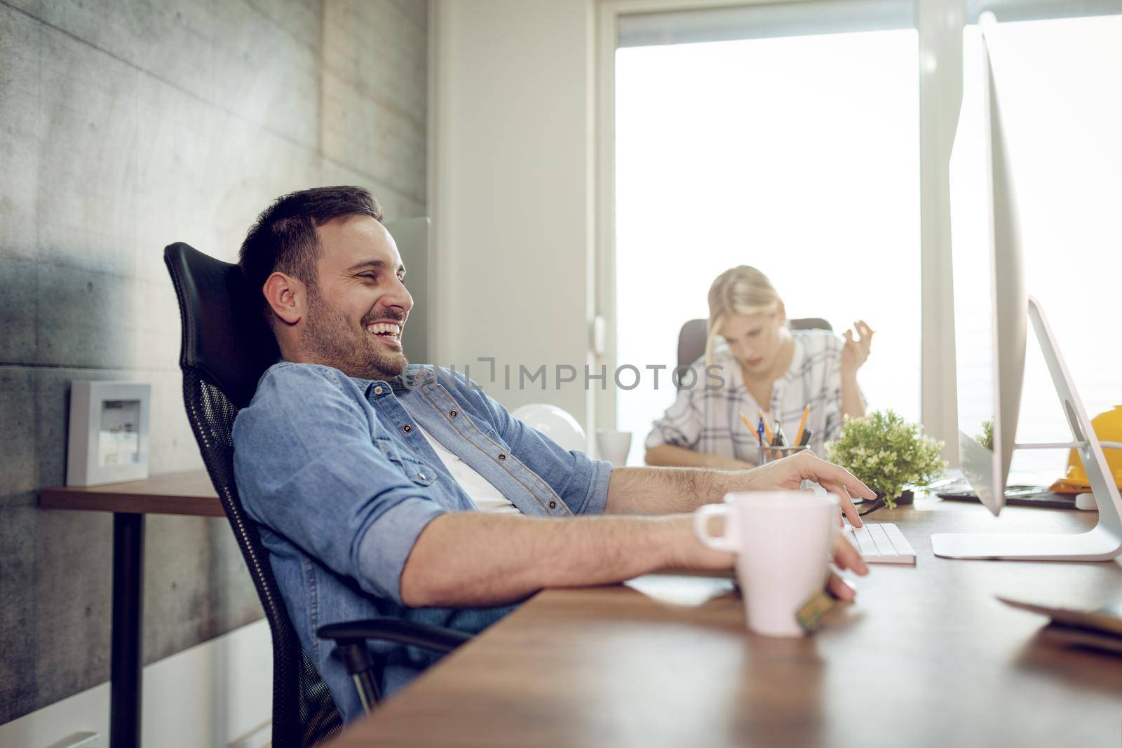 Young handsome successful freelance entrepreneur having fun and working on computer at the office. He is surfing on social media.