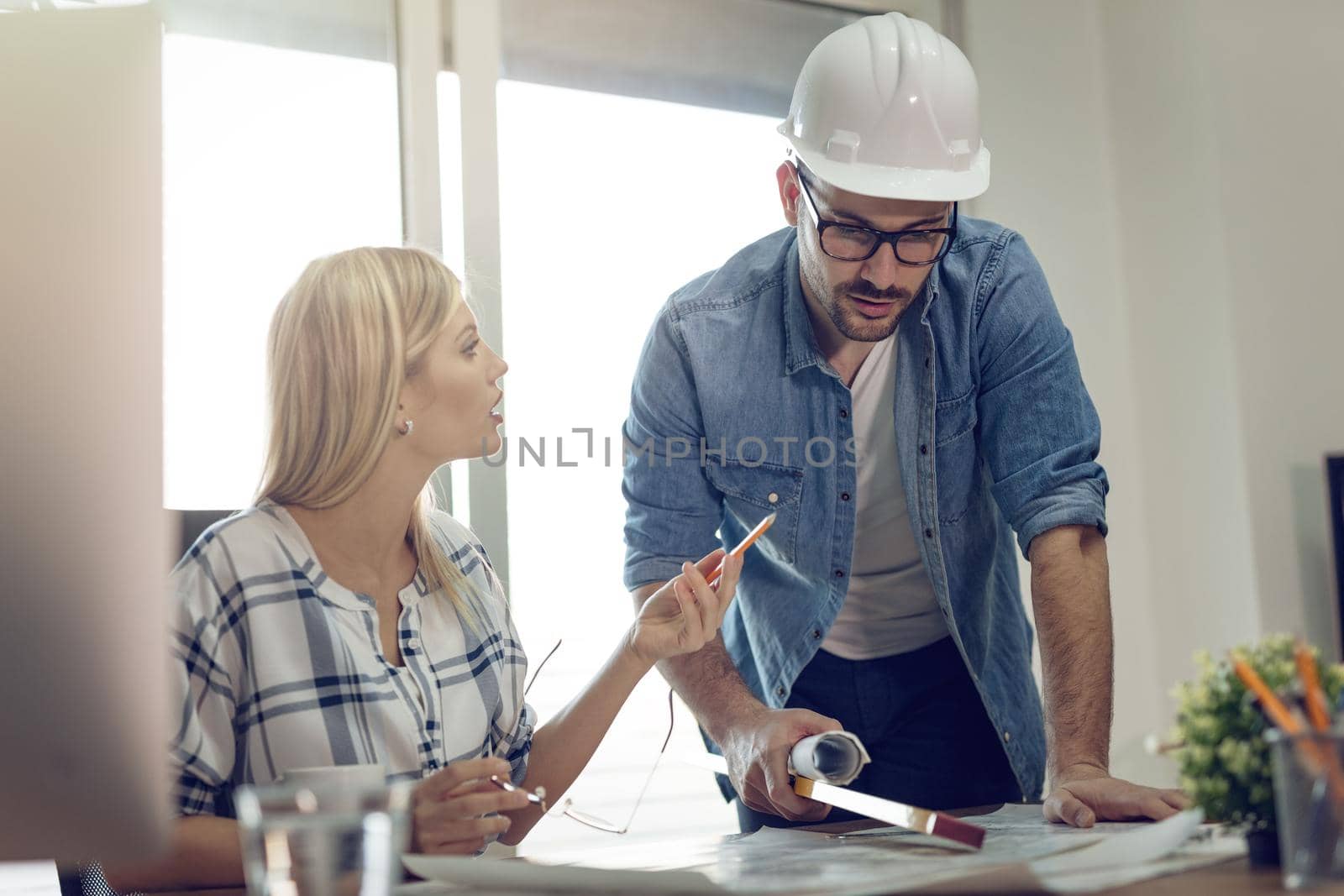 Young worried architect colleagues talking and analyzing blueprints while working on a new project at the office.