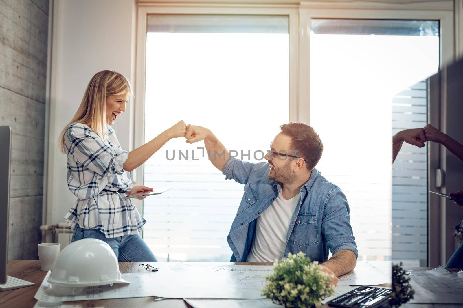 Young successful architect colleagues celebrating successful new project with fist bump at the office.