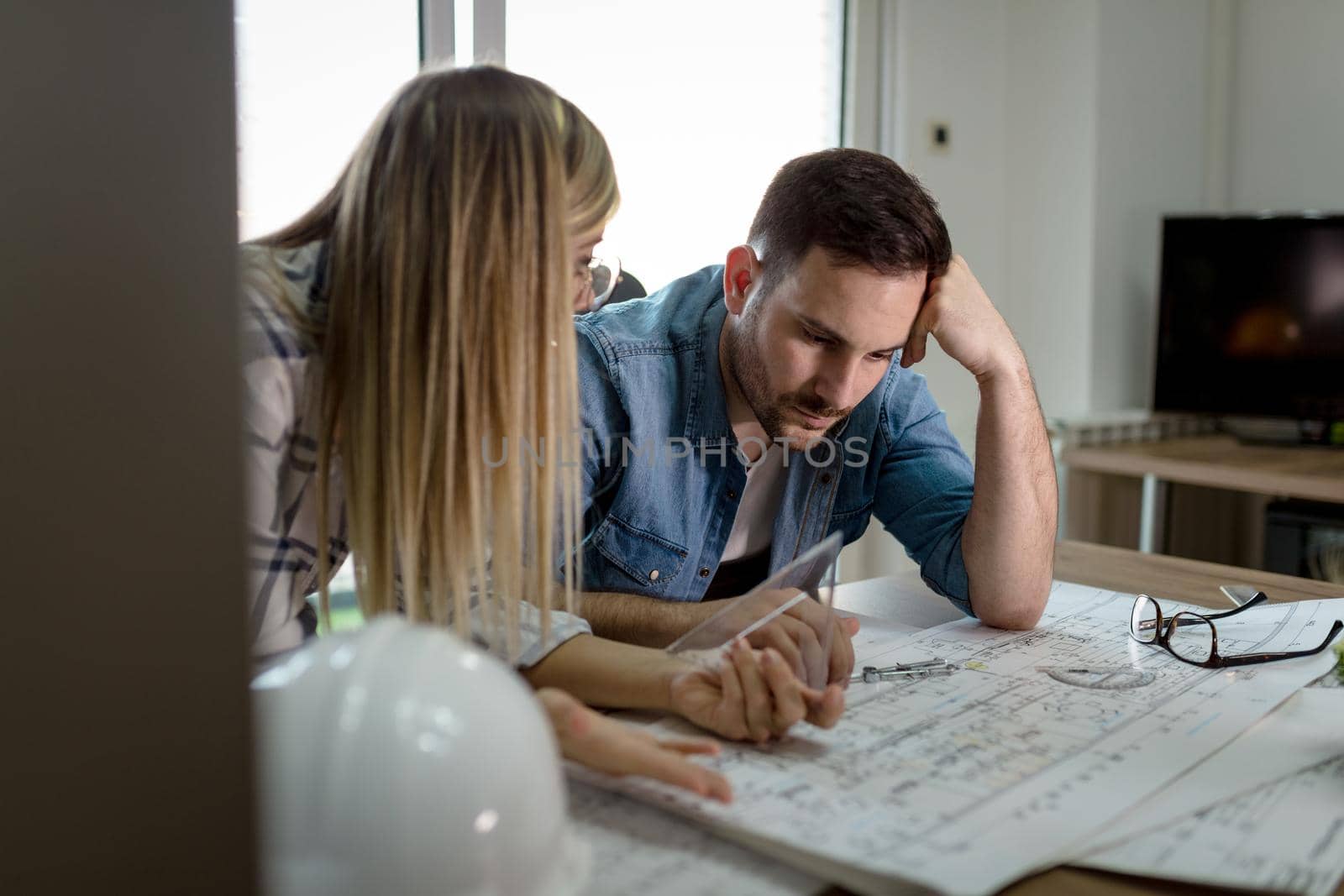 Young worried architect colleagues talking and analyzing blueprints while working on a new project at the office.