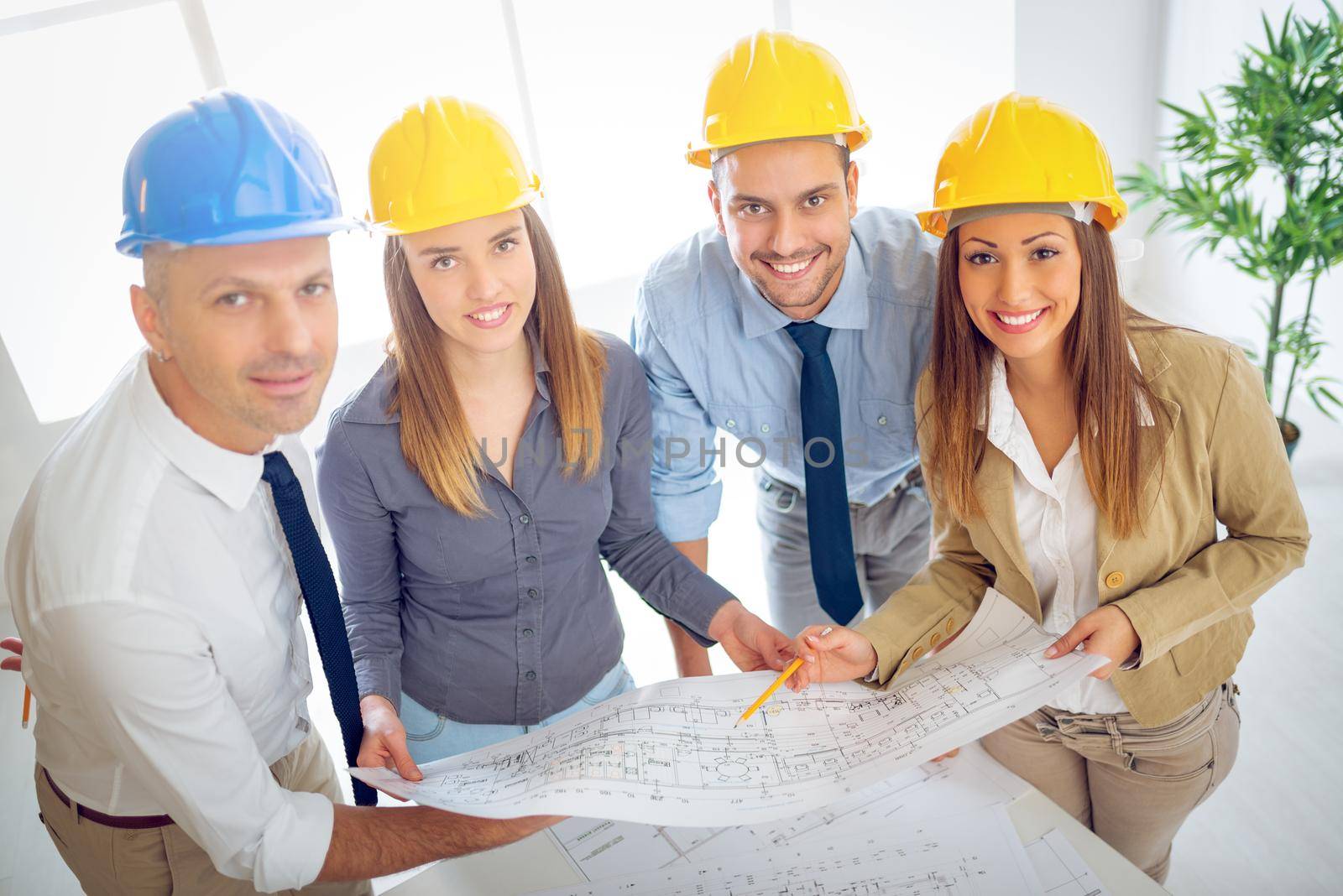 Successful young architects team discussing construction plans and planning what to change to be better. They are in the office. Looking at camera.
