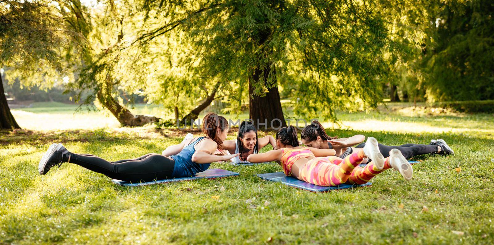 Four beautiful motivated female friends doing stretching exercise in the city park.