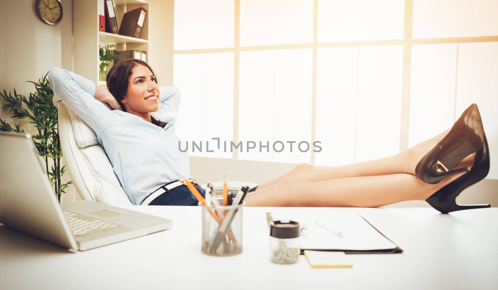 Attractive young woman stretching body and relaxing at the office with legs up on a desk. 