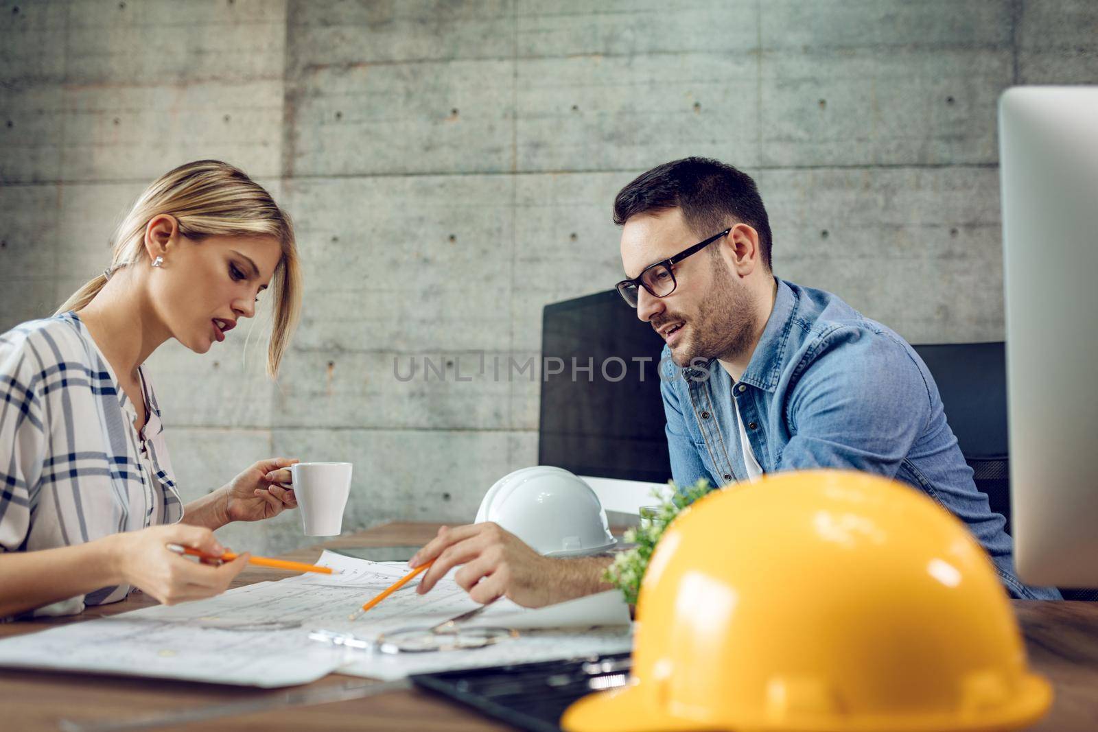 Young pensive architect colleagues analyzing blueprints and talking about him at the office.