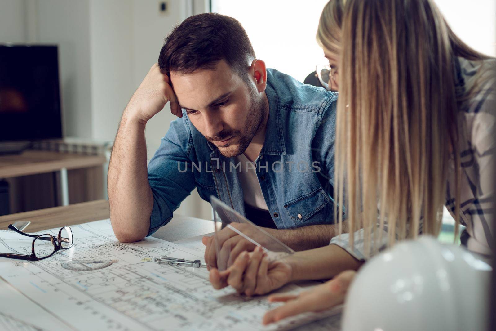 Young worried architect colleagues analyzing blueprints while working on a new project at the office.