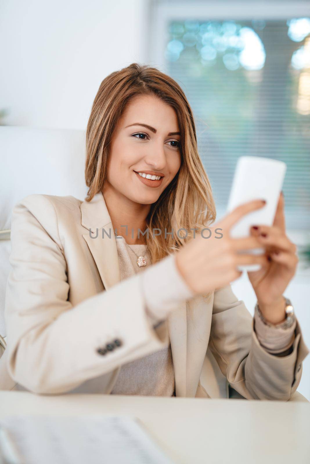 Young pretty smiling businesswoman texting message on the smartphone in the office. 