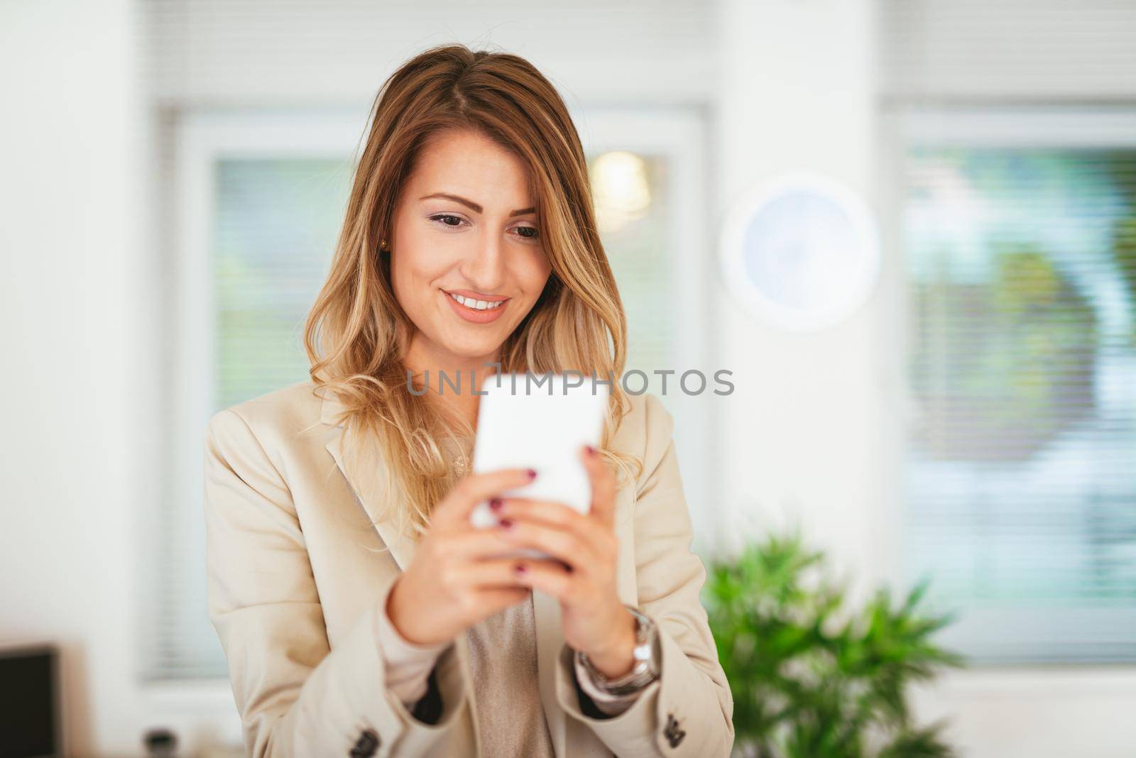 Young pretty smiling business woman texting on the smartphone in the office. 