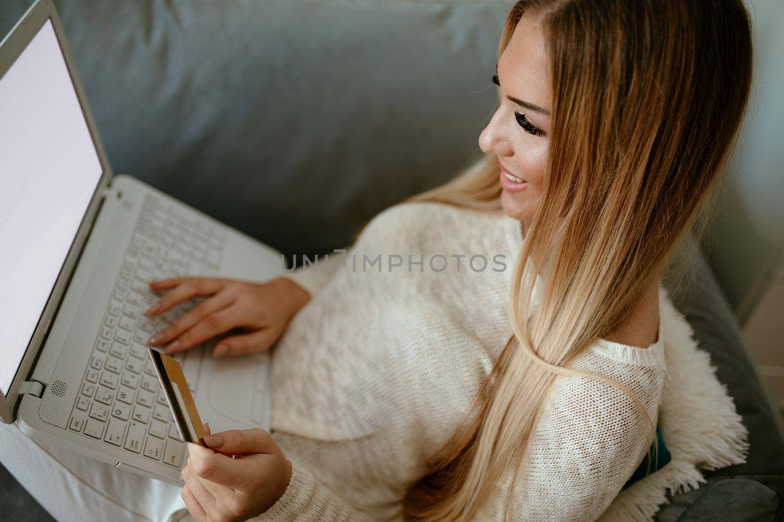 Attractive smiling girl sitting at her living room with credit card paying accounts by laptop. Selective focus.Top view.