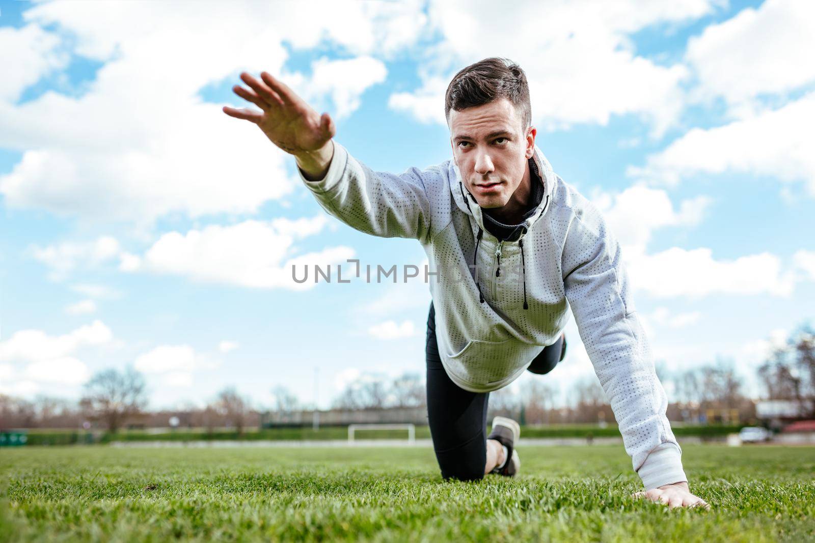 Active young man stretching and doing exercises in the public place on empty stadium. 