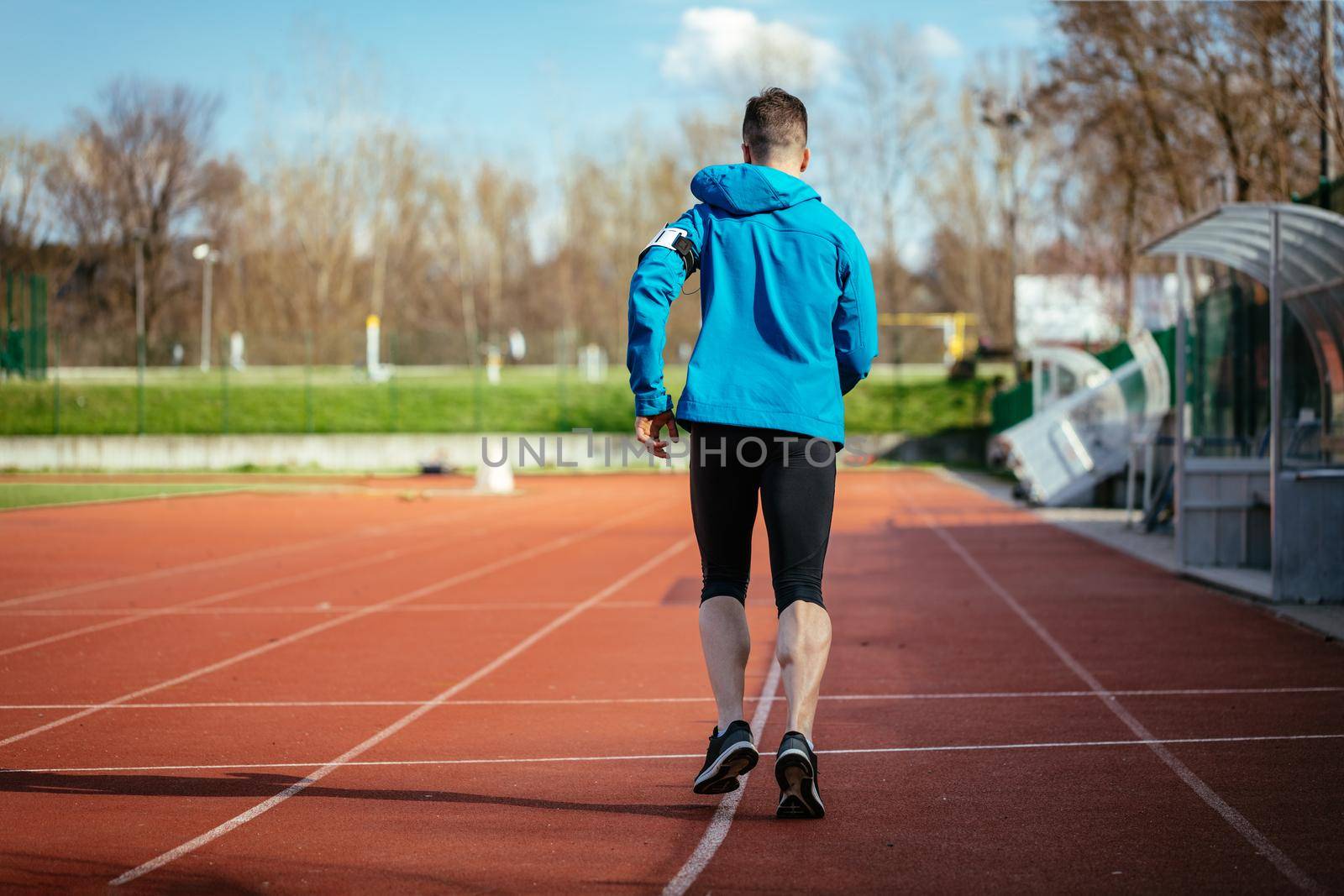 Rear view of athletic fit young sport man in full body length on tartan track on the stadium.