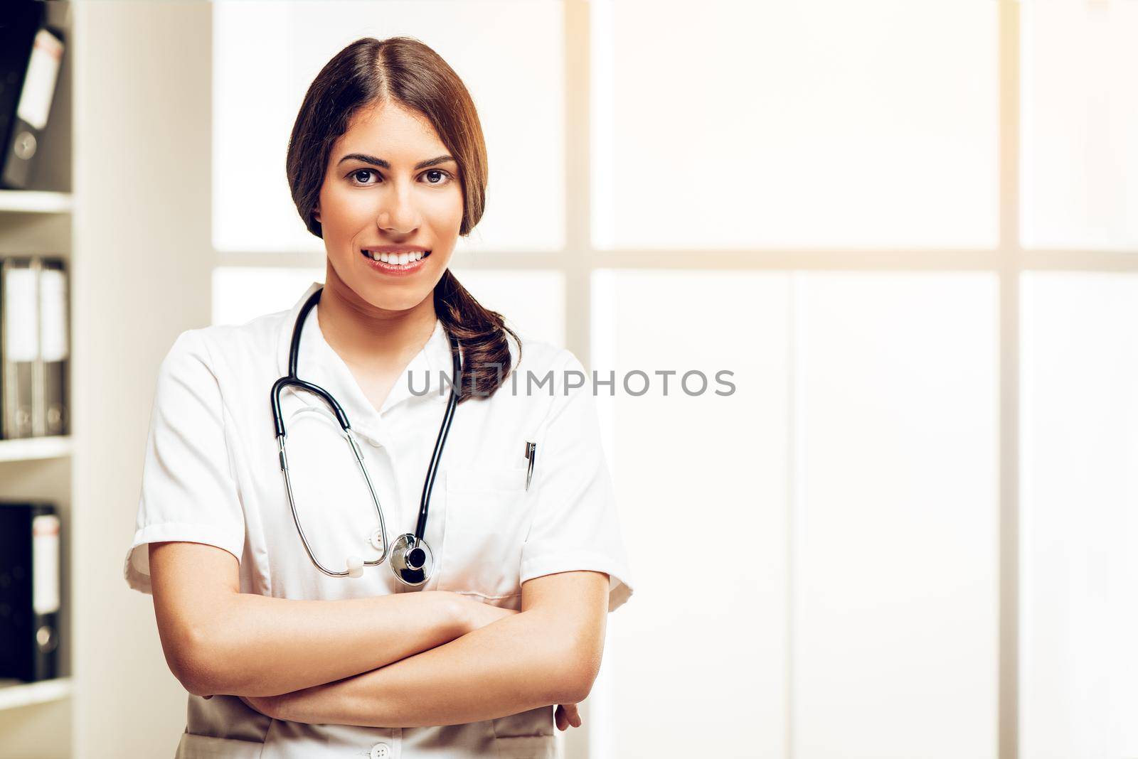 Portrait of a beautiful young female doctor standing in her consulting room, smiling and looking at camera.