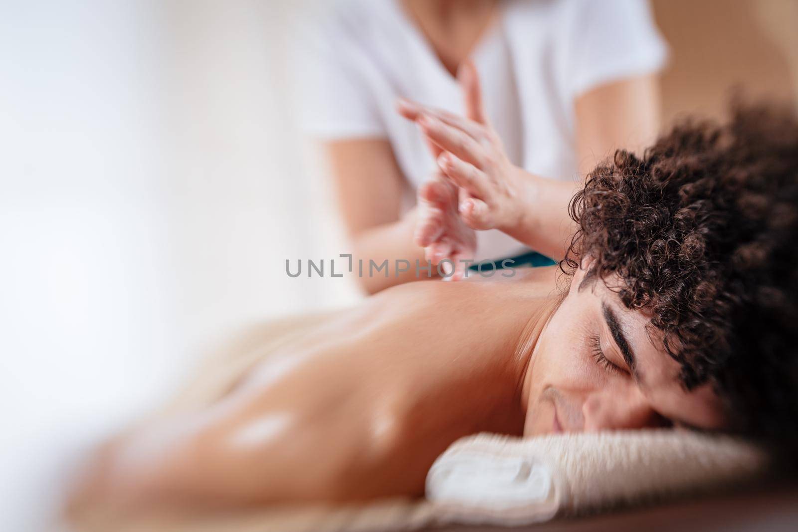 Close-up of a handsome healthy young man enjoying relaxing back massage at beauty salon. Selective focus.