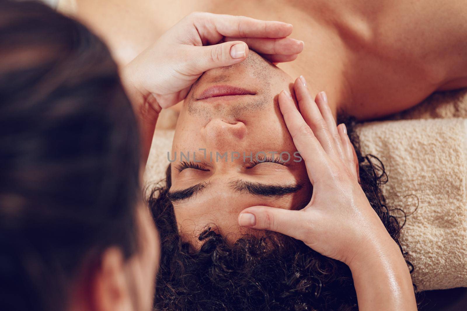 Close-up of a handsome healthy young man enjoying relaxing facial massage at beauty salon. Top view.