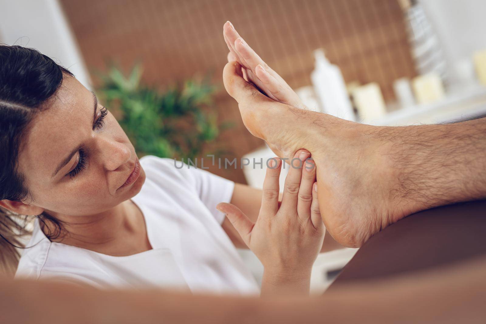 Close-up of a young female therapist massaging young man's foot at beauty salon.