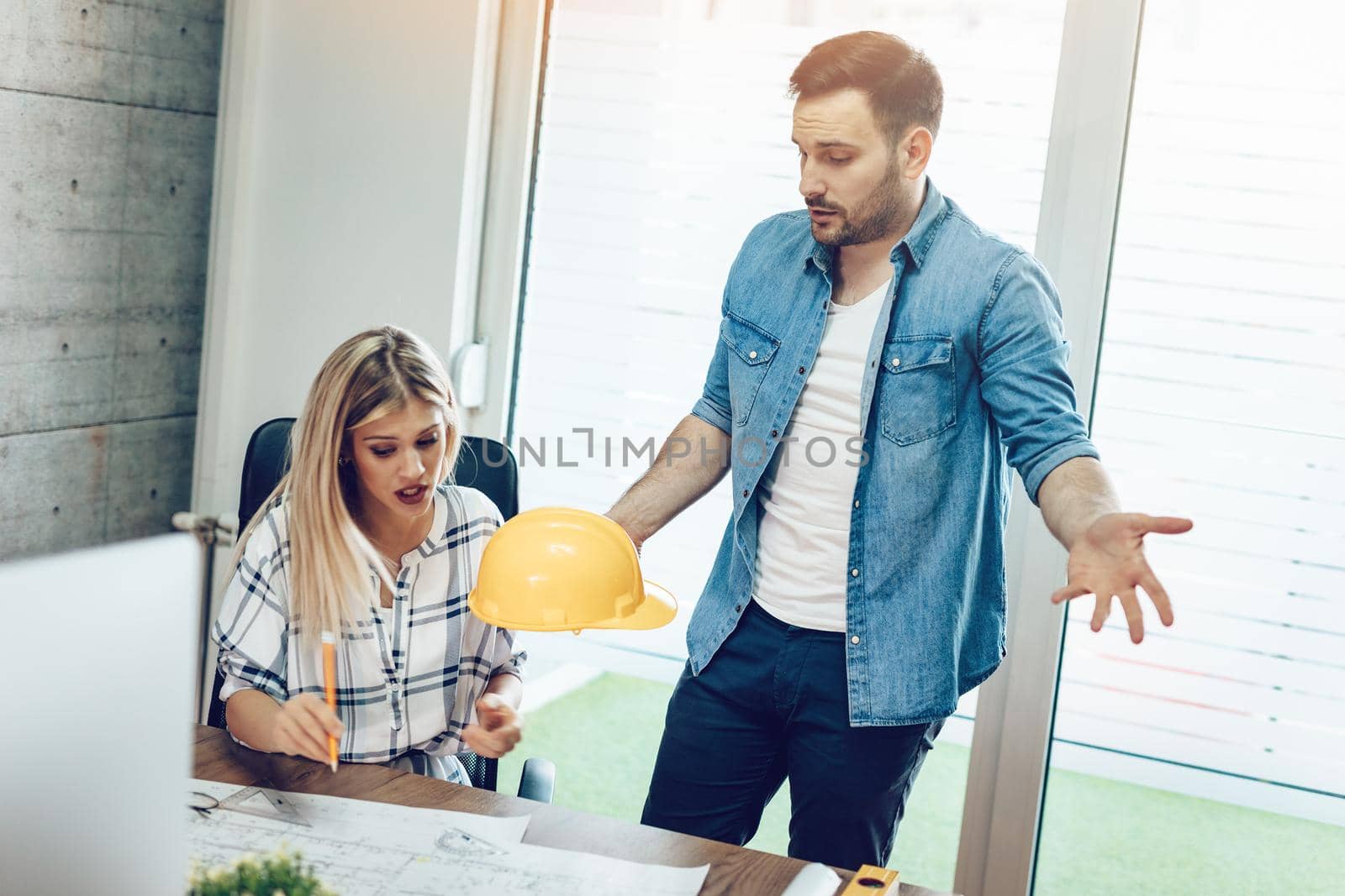 Young worried architect colleagues talking and analyzing blueprints while working on a new project at the office.